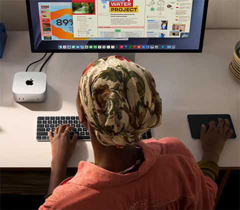 デスクでMac miniを使ってタイピングしている人物。Studio Displayが接続されている。Magic Keyboard、Magic Trackpad、様々なアイテムがある