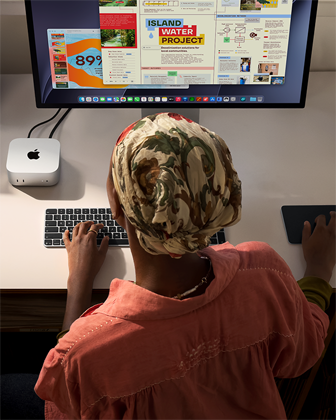 デスクでMac miniを使ってタイピングしている人物。Studio Displayが接続されている。Magic Keyboard、Magic Trackpad、様々なアイテムがある