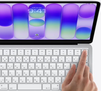 シルバーのMacBook Neo。ログイン画面が表示されていて、キーボードの右上角にあるTouch IDセンサーの上に指が置かれている