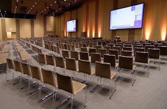 セミナー会場に多くの椅子が並んでいる様子。正面には2面の大型スクリーン。